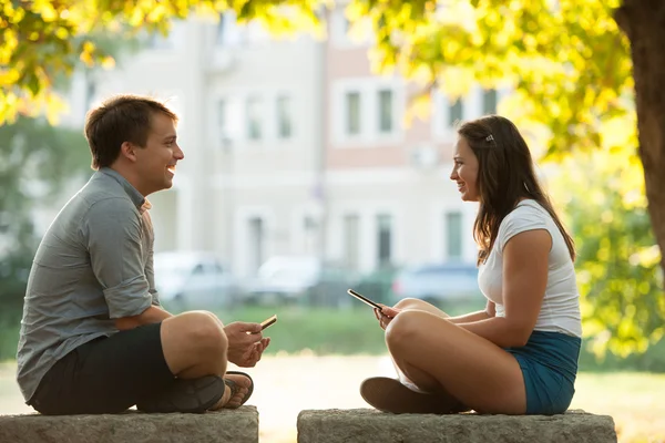 Pareja joven divirtiéndose en un banco en el parque mientras socializa ove — Foto de Stock