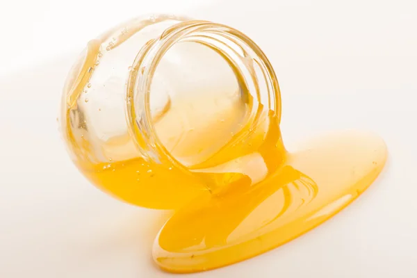 Sweet sticky golden honey flowing out of lying glass jar. — Stock Photo, Image