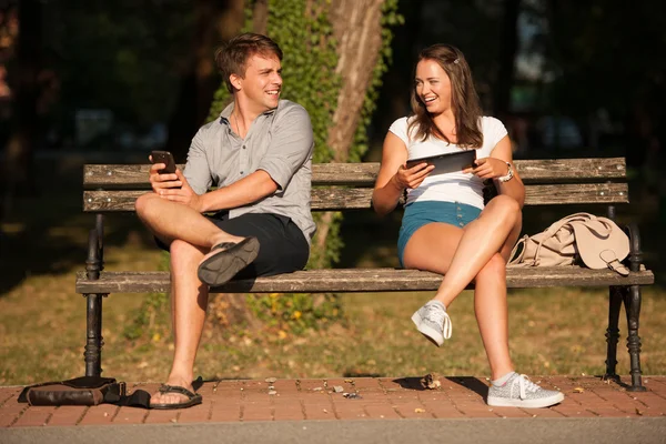 在公园的长凳上享受乐趣，同时社交奥雅纳对年轻夫妇 — 图库照片
