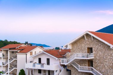 Herceg Novi, Karadağ, 30 Ağustos 2018. Gün batımında deniz ve dağların yanında fayanslı çatısı olan sahil evlerinin güzel manzarası.
