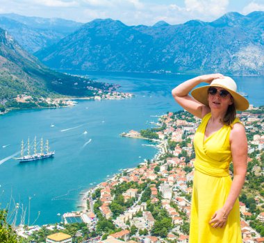 Güneş gözlüklü ve hasır şapkalı zarif bir kadın şehrin üzerinde poz veriyor.