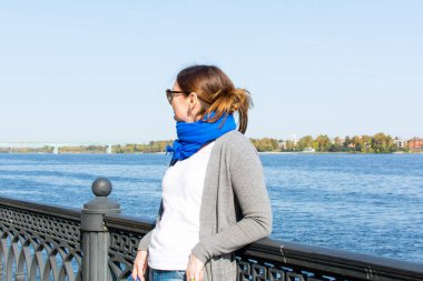 Yaroslavl. - Rusya. 20 Eylül 2020. Güneş gözlüklü ve kot pantolonlu güzel bir kadın nehrin kenarında duruyor..