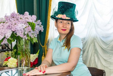 Zarif şapkalı güzel kadın masada oturuyor.