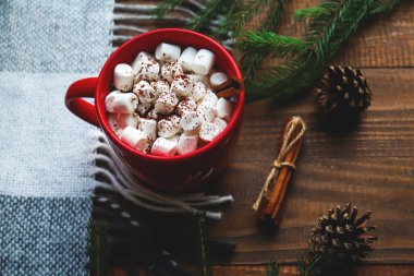 Ekoseli, çam kozalaklı ve köknar dallı, ahşap bir arka planda marşmelov ve tarçınlı kırmızı bardakta sıcak kakao. Sıcak kış konsepti. Yakın plan, seçici odaklanma. Noel sıcak içecekleri