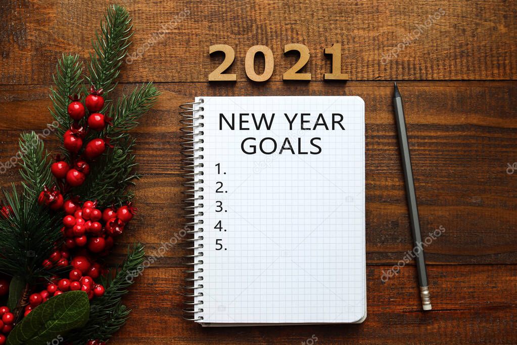 New Year goal list 2021. Christmas tree, red berries, pencil and notebook for writing goals or results of the year. Top view. Flat lay on wooden background. Festive, holiday and motivation concept.