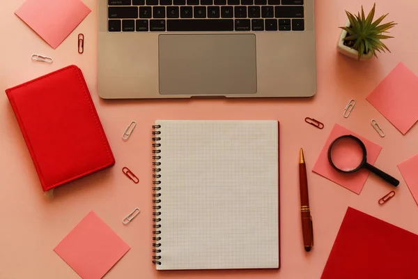 Trendy feminine workspace with laptop, plant, pen, open notebook, magnifying glass and sticky notes on pink background. Home office. Education and business concept. Top view, flat lay.