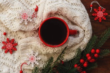 Sıcak kış kartpostalında kırmızı kahve, sıcak kış süveteri, Noel ağacı dalları ve kar taneleri oyuncakları var. Şenlikli, tatil konsepti. Üst manzara, düz uzanma.
