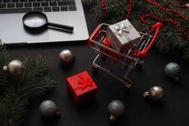 Noel online alışveriş konsepti. Hediyeler, dizüstü bilgisayar ve şenlikli arka planda büyüteçle market arabası. Kış tatilleri, indirimler ve sezon satışları. Yakın çekim, seçici odaklanma