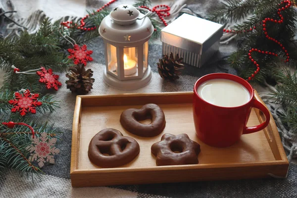 Sıcak kış kartpostalında kırmızı bir fincan süt, tepside zencefilli ekmek, Noel ağacı dalları, mumlu fener, hediye ve kar taneleri oyuncakları. Şenlikli Noel konsepti. Hygge tarzı
