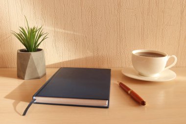 Ofis malzemeleriyle çalışma alanı. Not defteri, bitki, kalem ve kahve fincanı masaya. Ofis sabah konsepti.