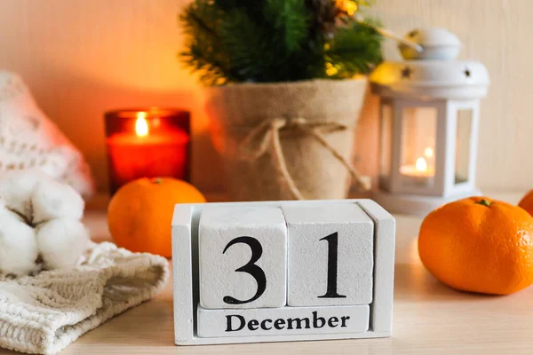 Tahta takvim tarihi 31 Aralık olan yeni yıl kompozisyonu. Mumlar, fener, Noel ağacı, takvim, örgü süveter ve mandalinalı güzel ev dekorasyonu kompozisyonu. Seçici odak.