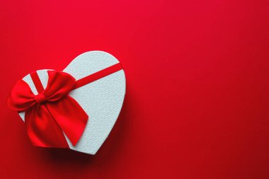 Sevgililer günü kartı. Kalp şeklinde hediye kutusu, kırmızı arka planda fiyonk ve fotokopi alanı. Üst manzara, düz uzanma.