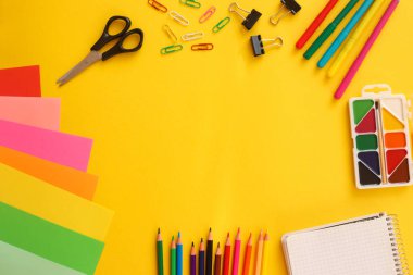 Okul konseptine geri dönelim. Renkli kâğıt, makas, kalemler, renkli kalemler, ataçlar ve parlak sarı arka planda boya ile düz yatıyordu. Uzayı metin için kopyala. Üst Manzara. Eğitim kavramı