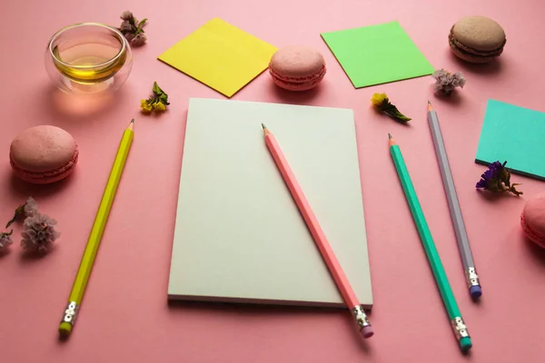 Espaço de trabalho feminino criativo com caderno de esboços para desenho, lápis, uma xícara de chá e macaroons em fundo rosa. Conceito de arte — Fotografia de Stock