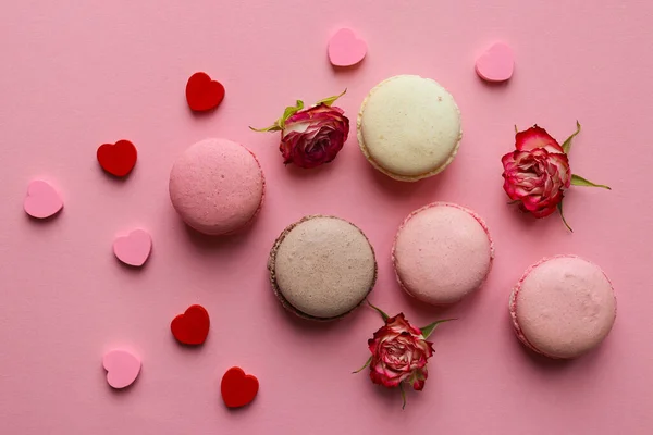 Concepto de San Valentín. Pasteles de macarrones franceses con flores y pequeños corazones sobre fondo rosa pastel. Enfoque selectivo, vista superior, plano —  Fotos de Stock