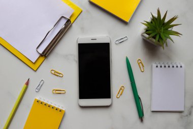 Workspace organization. Trendy workplace with notepads, smartphone, pencil, pen, and plant on marble background. Education and business concept. Top view, flat lay.