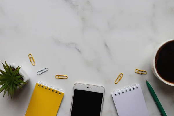 Modern ofis masası. Çalışma alanı, not defterleri, kalem, akıllı telefon, kahve ve açık gri mermer arka plan ve fotokopi alanı olan sulu bitki. Üst Manzara. Çalışma alanı organizasyonu. Düz yatıyordu.
