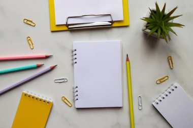 Sanatsal yaratıcı iş yeri. Not defterleri, çizim defterleri, kalemler, bitki, boş kağıtlı pano ve mermer zemin üzerinde çalışma alanı. Üst manzara, düz uzanma.