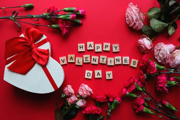 Ευχετήρια κάρτα για την ημέρα του Αγίου Βαλεντίνου. Η επιγραφή Happy Valentines Day από ξύλινα γράμματα, κουτί δώρου σε σχήμα καρδιάς και λουλούδια σε κόκκινο φόντο. Πάνω άποψη, επίπεδη lay — Φωτογραφία Αρχείου