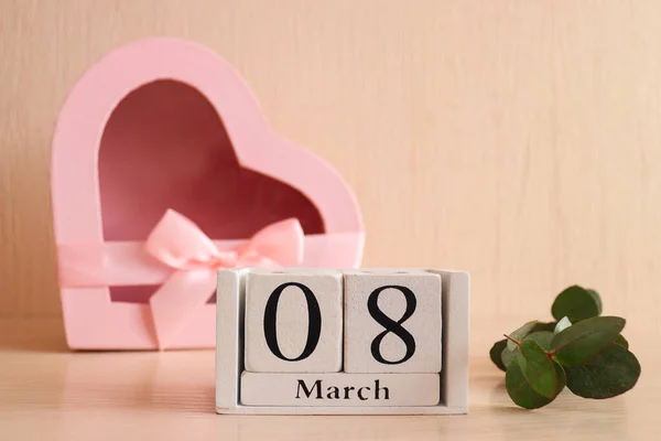 Ξύλινο ημερολόγιο 08 Μαρτίου, και ένα κουτί δώρου σε σχήμα καρδιάς. Όμορφη ευχετήρια κάρτα για την Ημέρα της Γυναίκας. Επιλεκτική εστίαση — Φωτογραφία Αρχείου