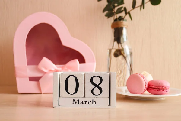 Όμορφη ευχετήρια κάρτα για την Ημέρα της Γυναίκας. Ξύλινο ημερολόγιο 08 Μαρτίου, ένα ποτήρι σαμπάνια, γαλλική μακαρονάδα ζαχαροπλαστικής και ένα κουτί δώρου σε σχήμα καρδιάς. Επιλεκτική εστίαση, κοντινό πλάνο — Φωτογραφία Αρχείου