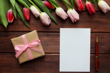 Kutlamalar için şablon. Koyu ahşap arka planda, içi boş kağıt ve kalemle dolu güzel bir lale buketi. Uzayı metin için kopyala. Üst manzara, düz yatış. Seçici odak, yakın plan.