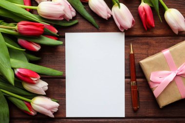 Kutlamalar için şenlikli bir maket. Koyu ahşap arka planda, içi boş kağıt ve kalemle dolu güzel bir lale buketi. Uzayı metin için kopyala. İlkbahar. Üst manzara, düz uzanma.