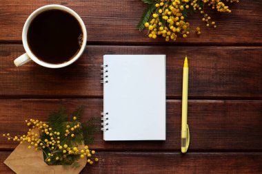 Kırsal yay, mimoza çiçekleri, boş not defterleri, sarı kalem ve bir fincan kahve ile süslenir. Üst görünüm, düz görünüm, kopyalama alanı.