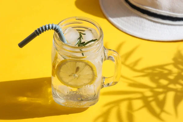 Yaz kompozisyonu. Buzlu ve limonlu soğuk limonata ve parlak sarı arka planda koyu palmiye gölgeli bir şapka. Yaz, tatil konsepti. Yakın plan..