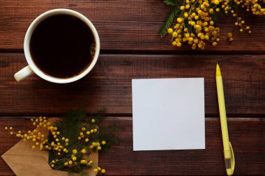 Kırsal yay, mimoza çiçekleri, boş kağıt, sarı kalem ve bir fincan kahve ile süslenir. Üst görünüm, düz görünüm, kopyalama alanı.