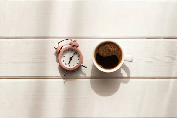 日陰のある木製のテーブルの上にコーヒーと目覚まし時計のカップ 目を覚ます 朝のコンセプト ミニマリズム トップビュー フラットレイアウト — ストック写真