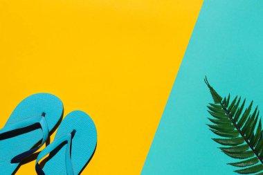 Bright summer background. Flip flops and palm leaf on yellow aquamarine background with copy space. Summertime and vacation concept. Hard light. Top view, flat lay