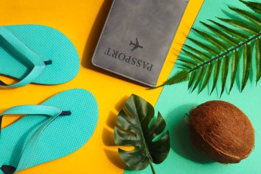 Tatil konsepti. Yaz kompozisyonu. Hindistan cevizi, canavar ve palmiye yaprakları, pasaport ve parlak sarı ve turkuaz arka planda parmak arası terlikler. Üst manzara, düz uzanma