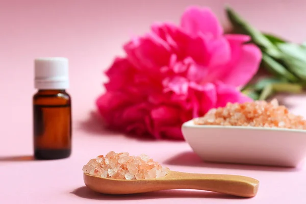 Beauty and spa concept. Pink himalayan salt close-up on a wooden spoon, essential oil and peony flower in the background. Selective focus — Stock Photo, Image