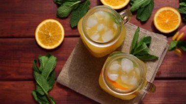 A womans hand adding a fresh bunch of mint into a fresh homemade citrus lemonade in jars on a wooden table. Summer refreshment drinks. Close-up, selective focus, top view