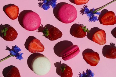 Yaz döngüsü. Pembe arka planda çilek, badem kurabiyesi ve çiçekler. Sert ışık. Üst manzara, düz uzanma