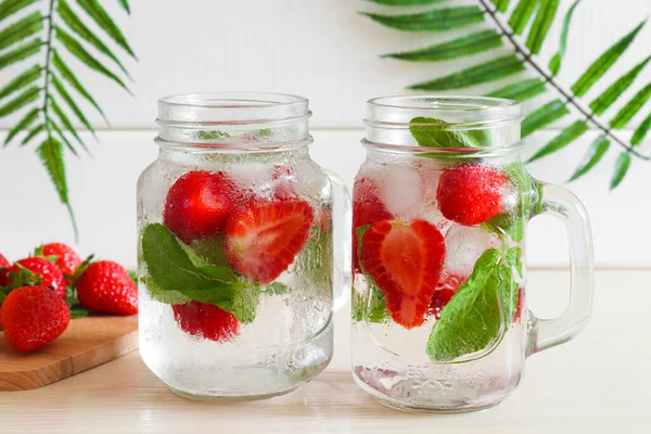 Fresh strawberry lemonade with ice and mint in two jars on the wooden table. Close-up, selective focus. Summer refreshment drinks. Thirst quencher concept