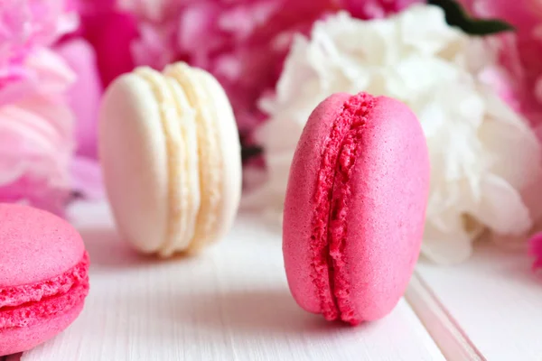 Cozy bakery and floral background. Close-up macarons and peonies on a white wooden table. Selective focus — Stock Photo, Image