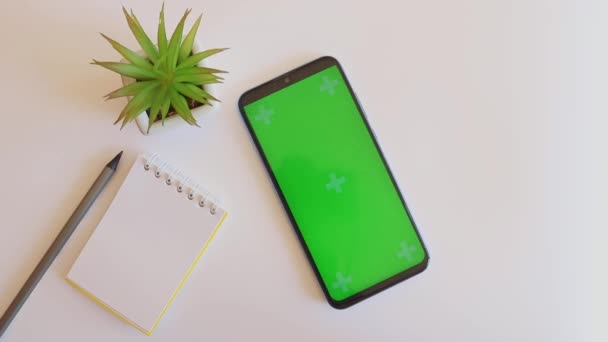 Bureau avec bloc-notes, crayon, plante et smartphone écran vert. Femme main met café sur la table de travail — Video