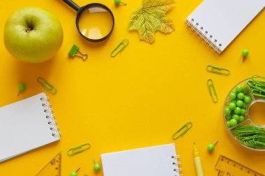 Kopya alanı olan farklı okul malzemelerinin çerçevesi. Not defterleri, kalem, ataç, cetvel, büyüteç ve sarı arka planda yeşil elma. Okul konseptine geri dönelim. Üst görünüm