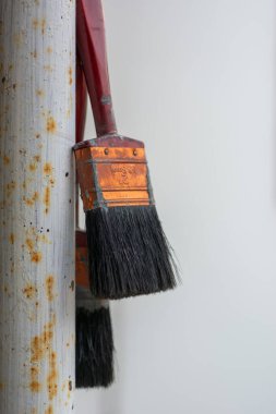 Old paint brush hangs on rusty iron pole.