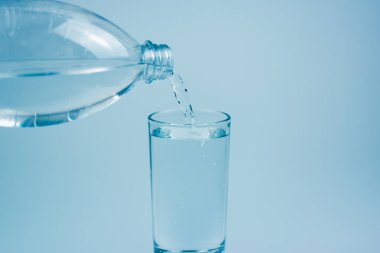 Pouring drink water into glass on light blue background.