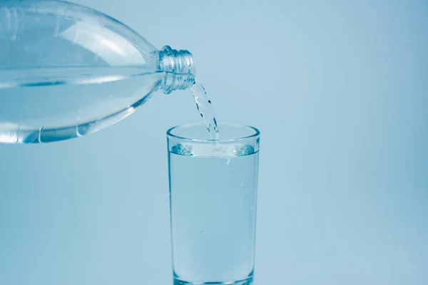 Pouring drink water into glass on light blue background.