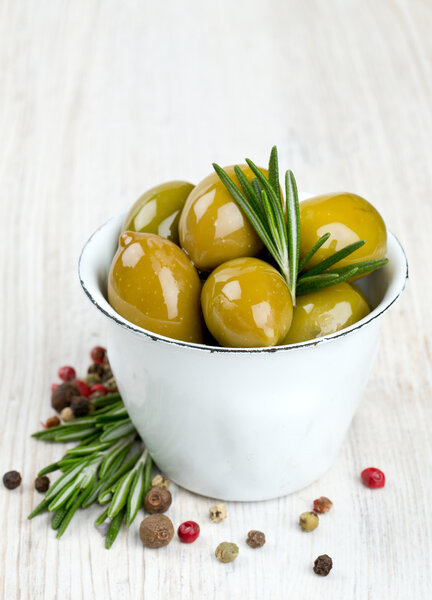 green olives in a metallic cup on wooden surface