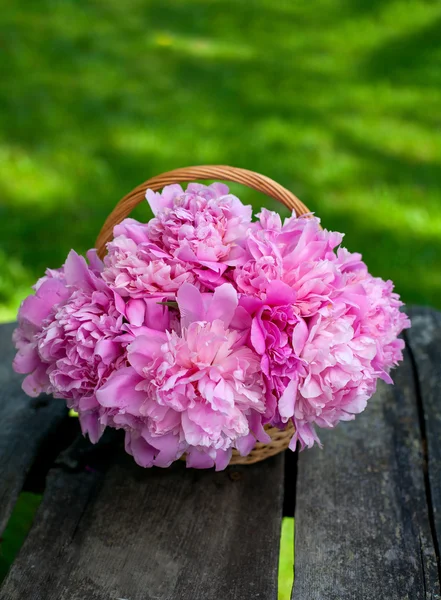 Ahşap zemin üzerinde bir sepet içinde peonies demet — Stok fotoğraf