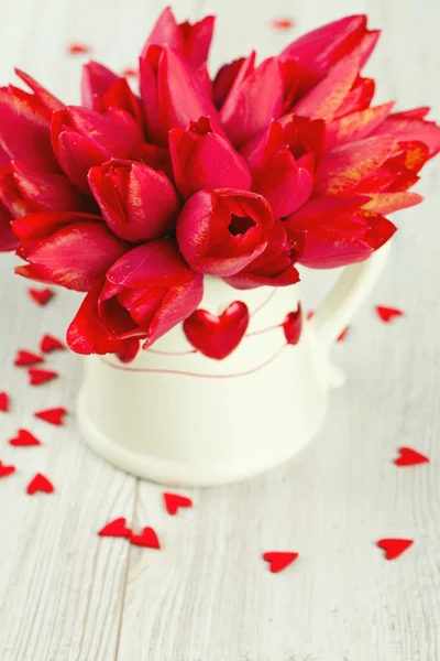 Bouquet of red tulips in a pitcher and scattered wooden hearts — Stock Photo, Image