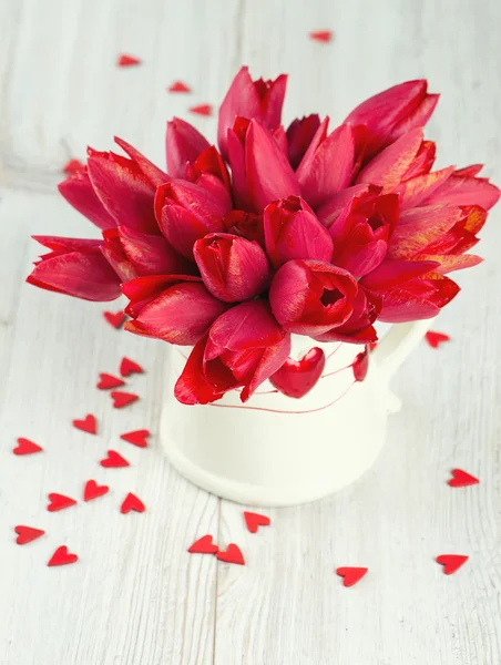 Boeket van rode tulpen in een kruik en verspreide houten harten — Stockfoto