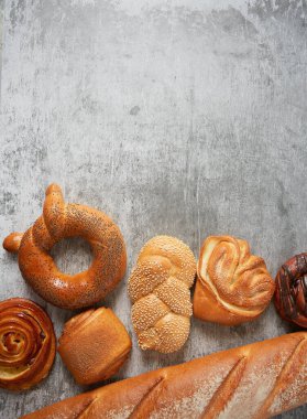 Gri yüzeyde taze çörekler. Fırın konsepti. Metnin için susam, çikolata ve tarçınlı çörek ve fotokopi alanı.