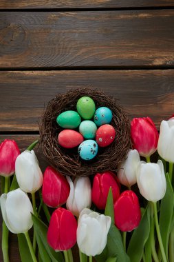 Kahverengi ahşap yüzeyde renkli laleler ve Paskalya yumurtaları