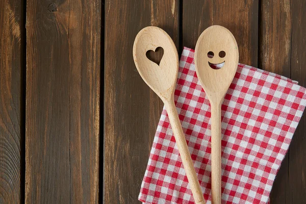 Two wooden spoons on brown wooden surface. Cooking concept. Spoons are with a smile and heart on it.